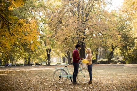 Multiracial couple with bicycle standing in the autumn parkの写真素材