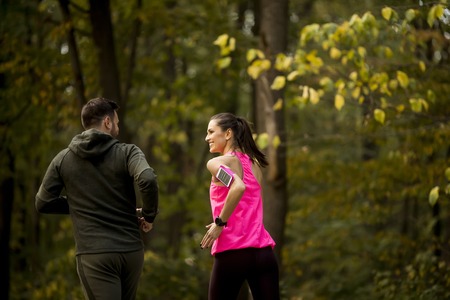 Athletic couple running together on the forest trail in autumnの写真素材