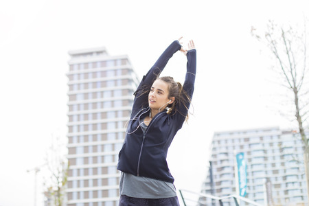 Pretty young woman with earphones stretching during sport training in urban enviroment