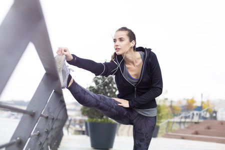 Pretty young woman with earphones stretching during sport training in urban enviromentの写真素材