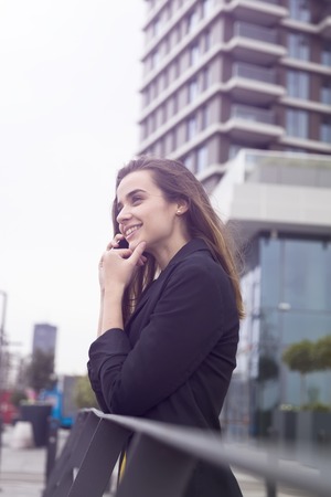 Young business woman uses cellphone at the street against office buildingの写真素材