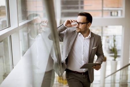 Happy businessman dressed in suit standing  in modern office  and using tabletの写真素材