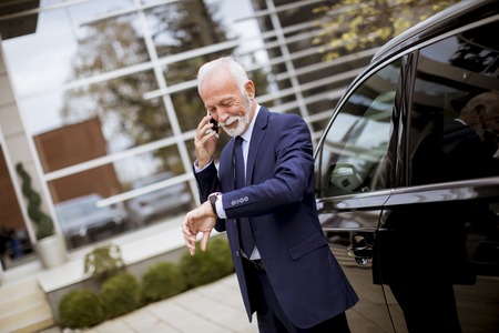 Portrait of senior businessman using mobile phone near carの写真素材