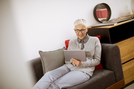 Pretty senior businesswoman sitting with tablet on sofa