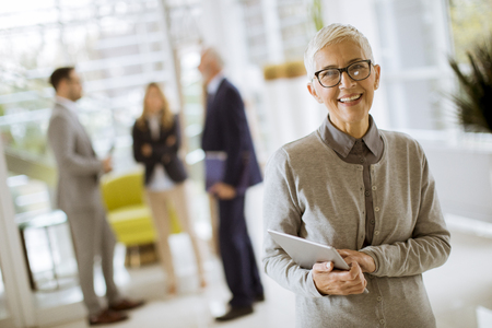 Portrait of senior businesswoman standing with digital tablet while other business people standing in backgroundの写真素材