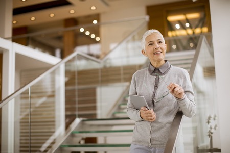 Portrait of senior businesswoman standing in modern office and holding digital tabletの写真素材