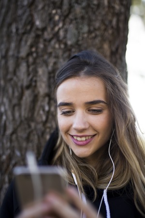 Portrait of a happy girl listening music on line with wireless headphones from a smartphone  against treeの写真素材