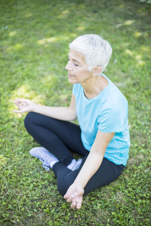 Senior woman meditating in the park on grassの写真素材