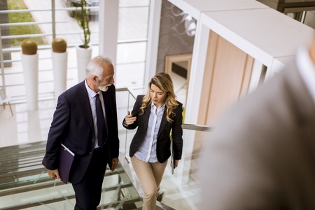 Senior businessman and businesswoman walking and taking stairs in an office buildingの写真素材