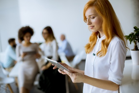 Pretty young red hair woman using digital tablet in the modern officeの写真素材