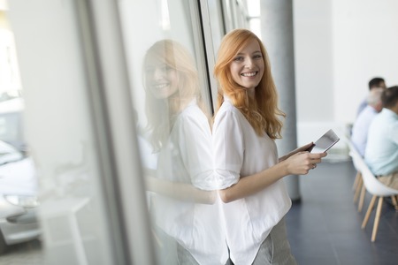Pretty young red hair woman using digital tablet in the modern officeの写真素材