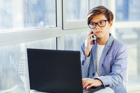 Portrait of teen boy talking over mobile phone and using laptop