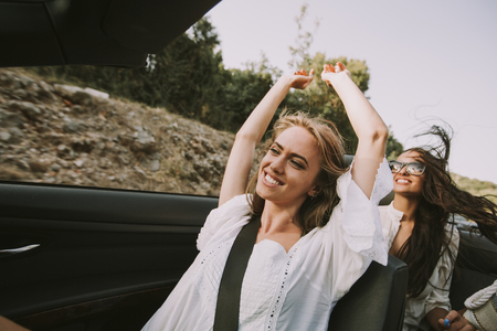 Two happy female friends driving in white cabriolet car and looking for freedom and funの写真素材