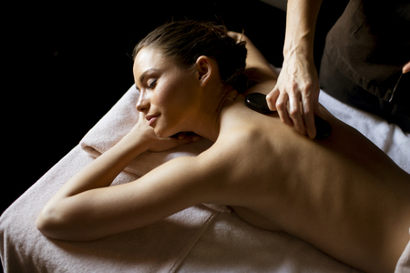 Beautiful young woman having her shoulder and body massaged with a hot stones by a professional masseur at a spa centerの写真素材