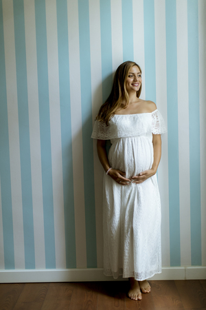 Pretty young pregnant woman standing by the wall in the roomの写真素材