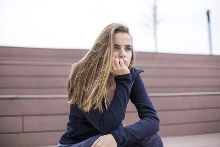 Portrait of worried, sad and depressing young woman sits outsideの写真素材