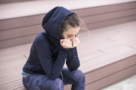 Portrait of worried, sad and depressing young woman sits outsideの写真素材