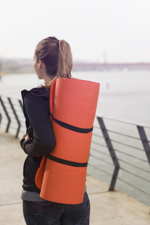 Fitness woman walking with mat on back outdoorの写真素材