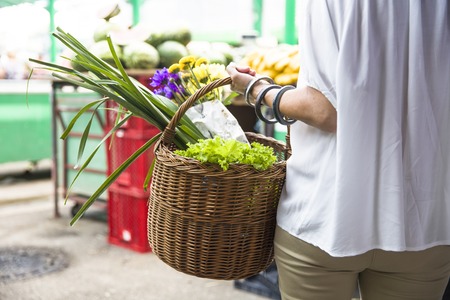 Senior woman holds basket with flowers and vegetables walks at marketの写真素材