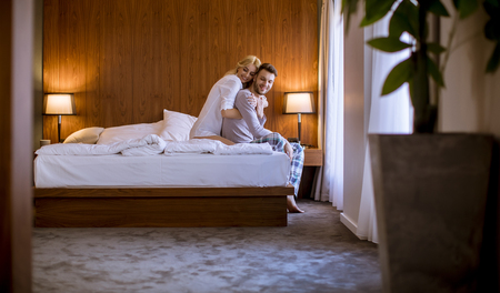 Loving and hugged young couple sitting on the bed in the bedroomの写真素材