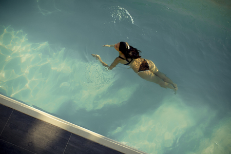 Aerial view of swimming woman floating in swimming pool at summer dayの写真素材