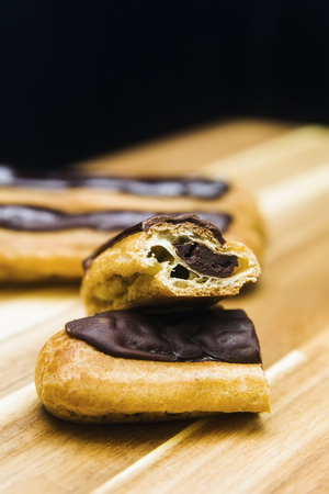 Eclair crispy creamy cake with dark chocolate isolated on wooden background