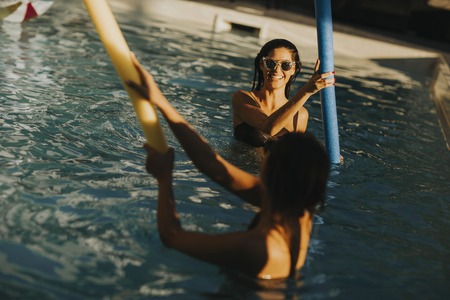 Young women having fun with swimming pool noodles at hot summer dayの写真素材
