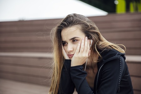 Sad and frustrated sporty young woman sitting alone outdoorの写真素材