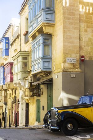 VALLETTA, MALTA - NOVEMBER 18, 2018: Old stone houses with colorful windows and black and yellow classic style Bentley car on the street of Valletta, Malta.のeditorial素材