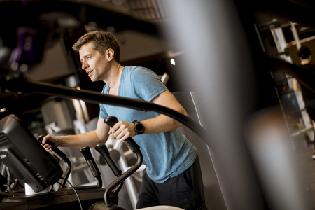 Young man doing exercise on elliptical cross trainer in sport fitness gym clubの写真素材