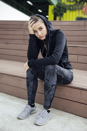 Sad and frustrated sporty young woman sitting alone outdoor