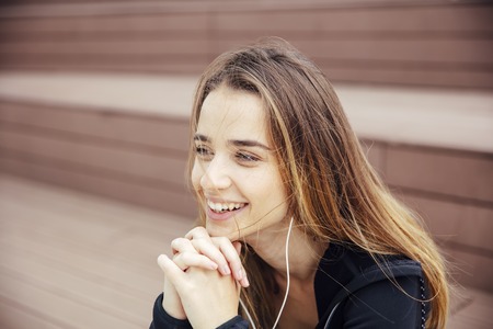Smiling young woman with smartphone and headphones listening to music outdoor