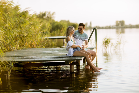 Loving couple sitting on the pier on lake at summer sunsetの写真素材