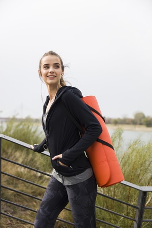 Young fitness woman walking with mat on back outdoor