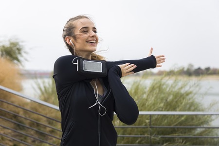 Female young athlete stretching her arms  while listening to music outdoors