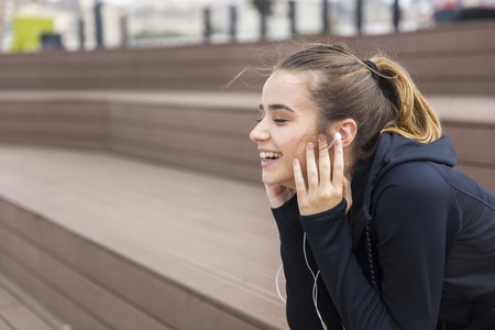 Smiling young woman with smartphone and headphones listening to music outdoorの写真素材