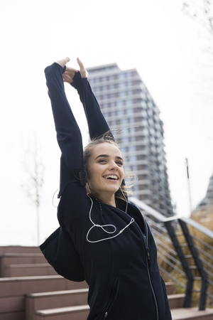 Female young athlete stretching her arms  while listening to music outdoorsの写真素材