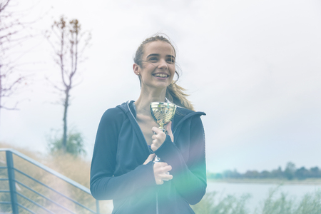 Happy sporty young woman holding gold trophy cup outdoorの写真素材