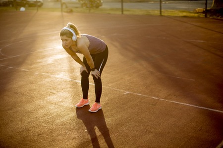 Pretty young female resting after an active fitness training while standing on the playground at sunsetの写真素材