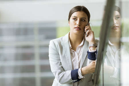 Pretty young business woman stands on the stairs at the office and use mobile phoneの写真素材
