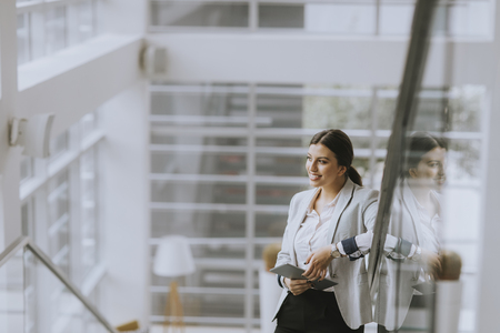 Pretty young business woman stands on the stairs at the office and use mobile phoneの写真素材