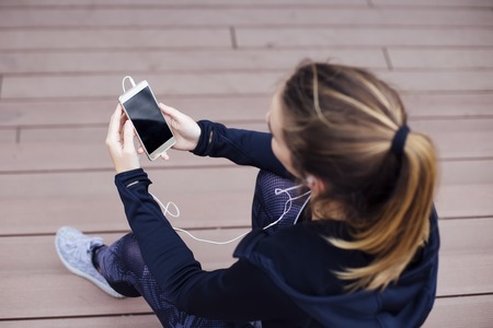 Young sporty woman using cellphone and sittinng on stairs outdoorsの写真素材