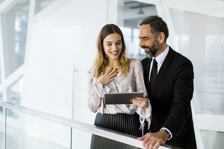 Handsome smiling mature businessman and his cute young female coworker with digital tablet in the modern officeの写真素材