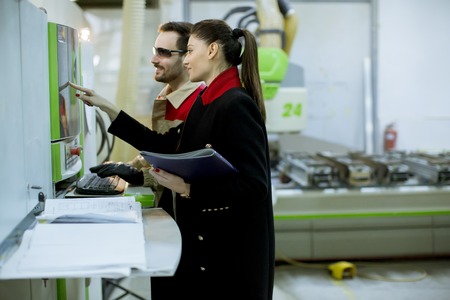 Pretty young woman controlling process in the factory with male worker