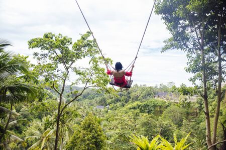 Young tourist woman swinging over the tropical rainforest at Bali island, Indonesia