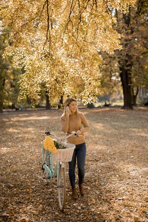 Pretty young woman with bicycle using smartphone in autumn park