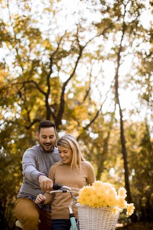 Active young couple enjoying together in riding bicycle at golden autumn parkの写真素材