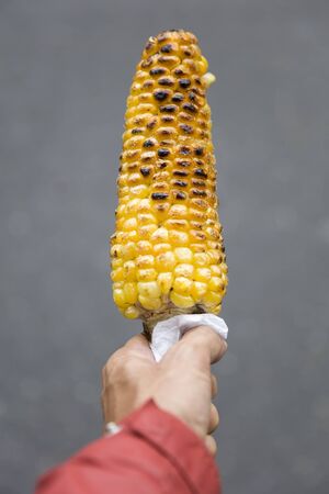 Closeup of the grilled corns in hand on the streetの写真素材