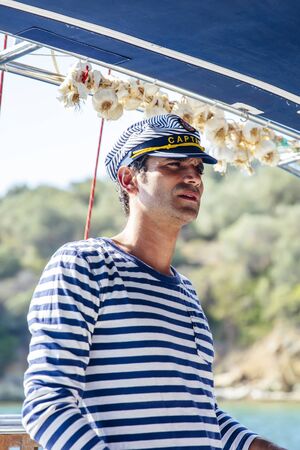 Handsome young man with captain cap on a sailboat at sea on a suuny day