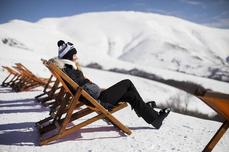 Young woman skier relaxing in a lounge chair after skiing in the mountains in winterの写真素材